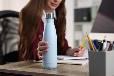 Photo of Woman holding thermos bottle at workplace, closeup