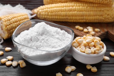 Photo of Bowl with corn starch and kernels on dark wooden table, closeup