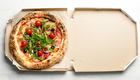 Photo of Tasty pizza with meat and arugula in cardboard box on white table, top view