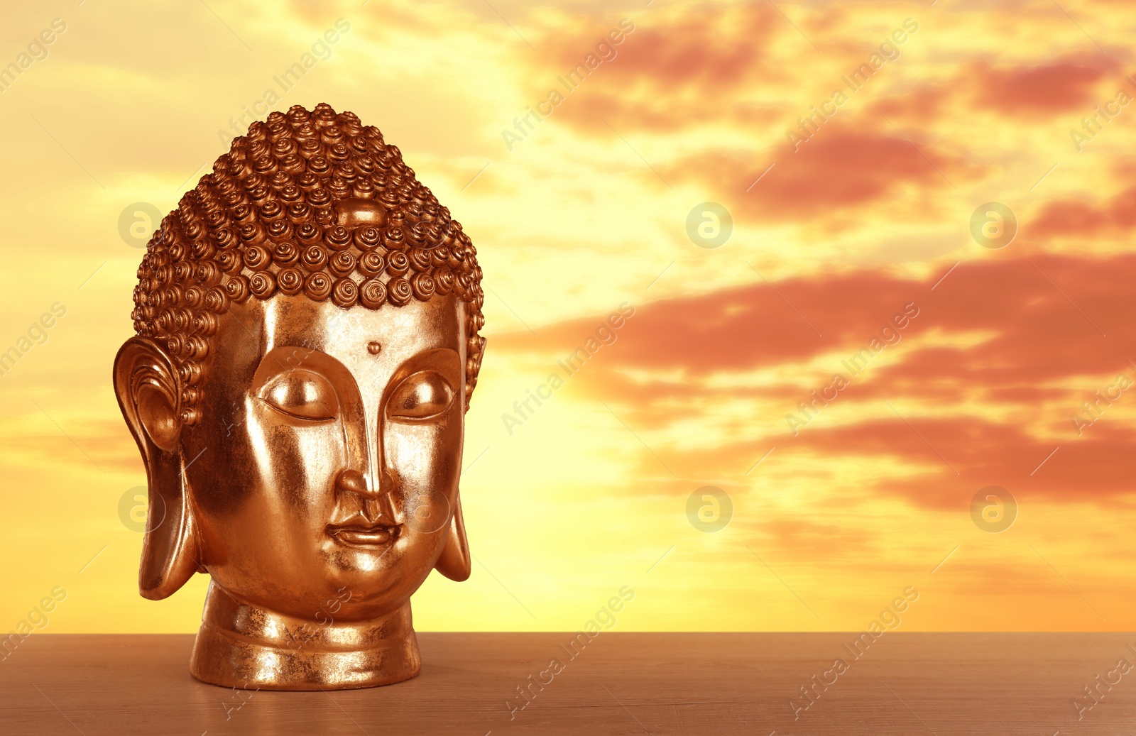 Image of Beautiful golden Buddha sculpture on wooden surface at sunset. Space for text