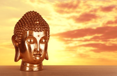 Image of Beautiful golden Buddha sculpture on wooden surface at sunset. Space for text