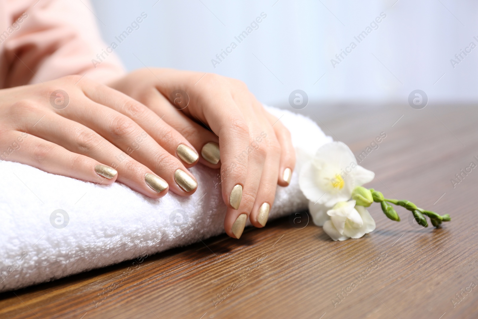 Photo of Woman with gold manicure on rolled towel at table, closeup. Nail polish trends