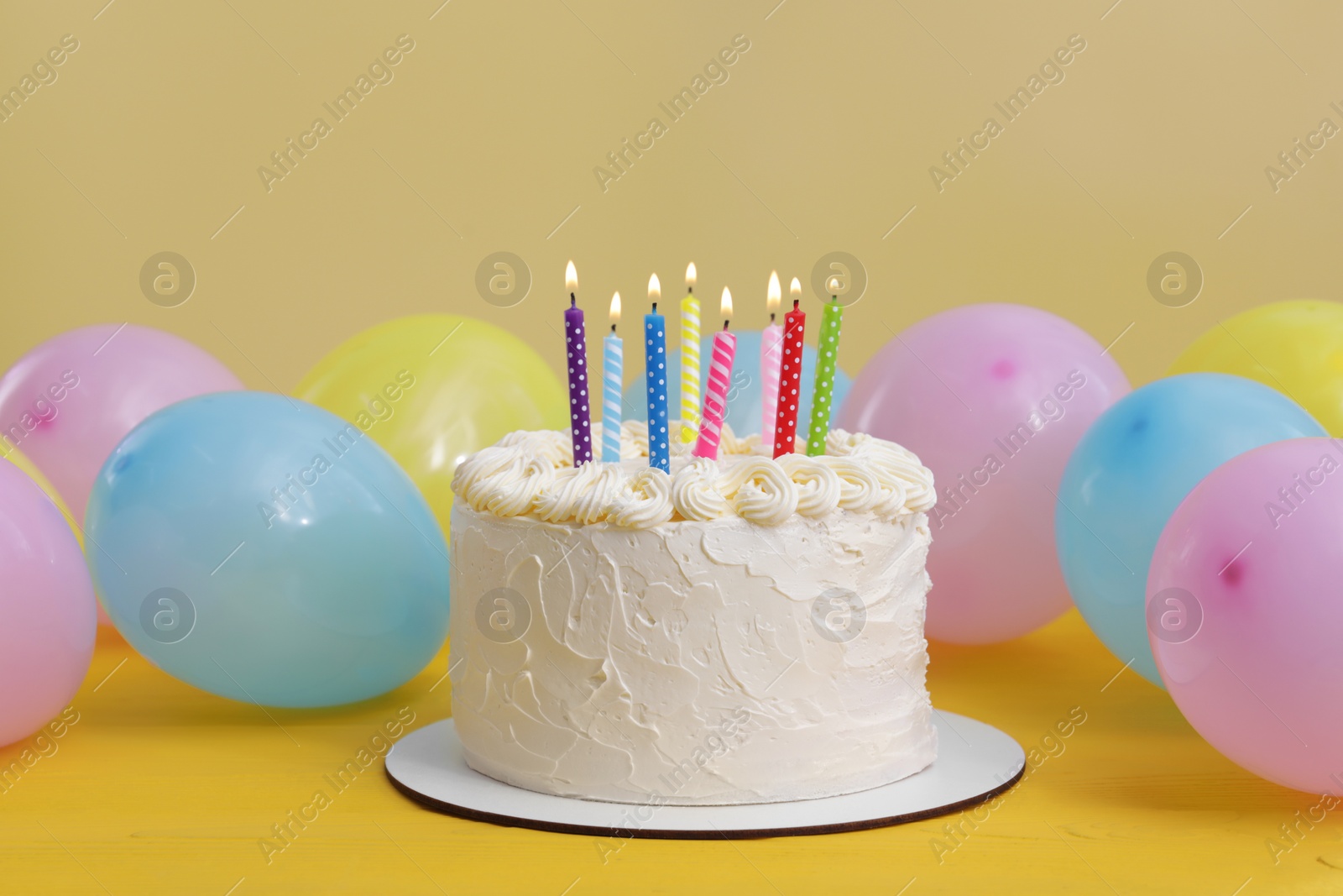 Photo of Delicious cake with burning candles and festive decor on yellow background