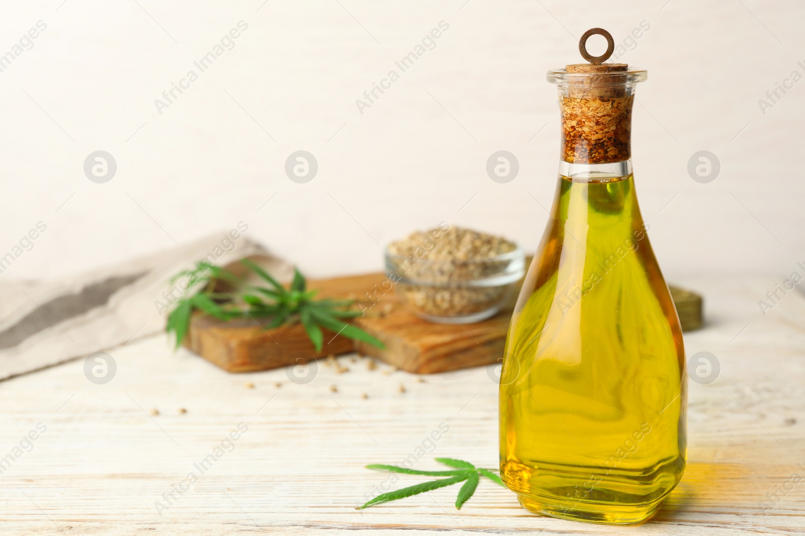 Photo of Bottle of hemp oil on white wooden table. Space for text