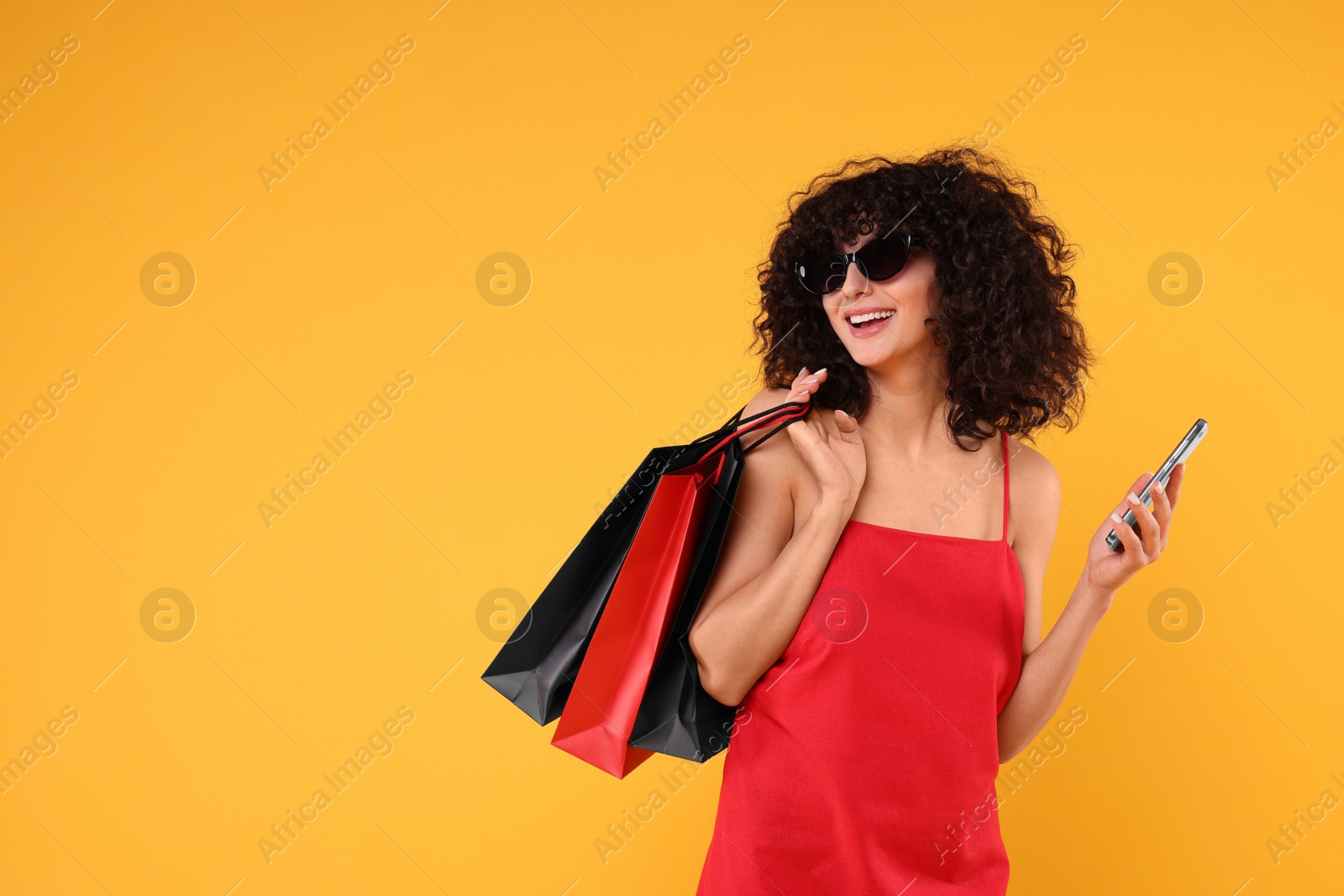 Photo of Happy young woman with shopping bags and modern smartphone on yellow background. Space for text