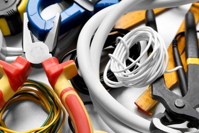 Photo of Different wires and electrician's tools on white table, closeup