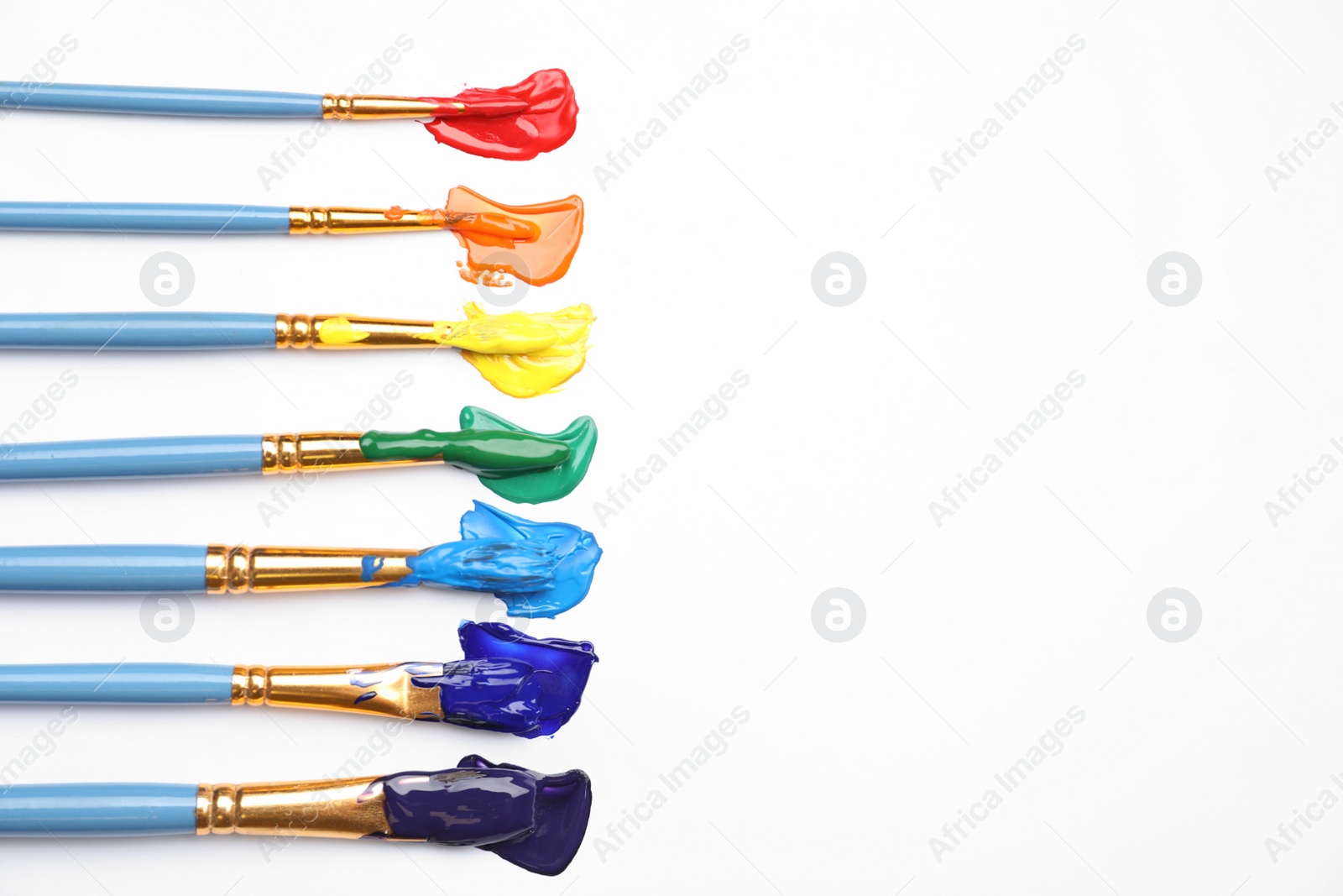 Photo of Set of brushes with different paints on white background, flat lay. Rainbow colors