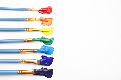 Photo of Set of brushes with different paints on white background, flat lay. Rainbow colors