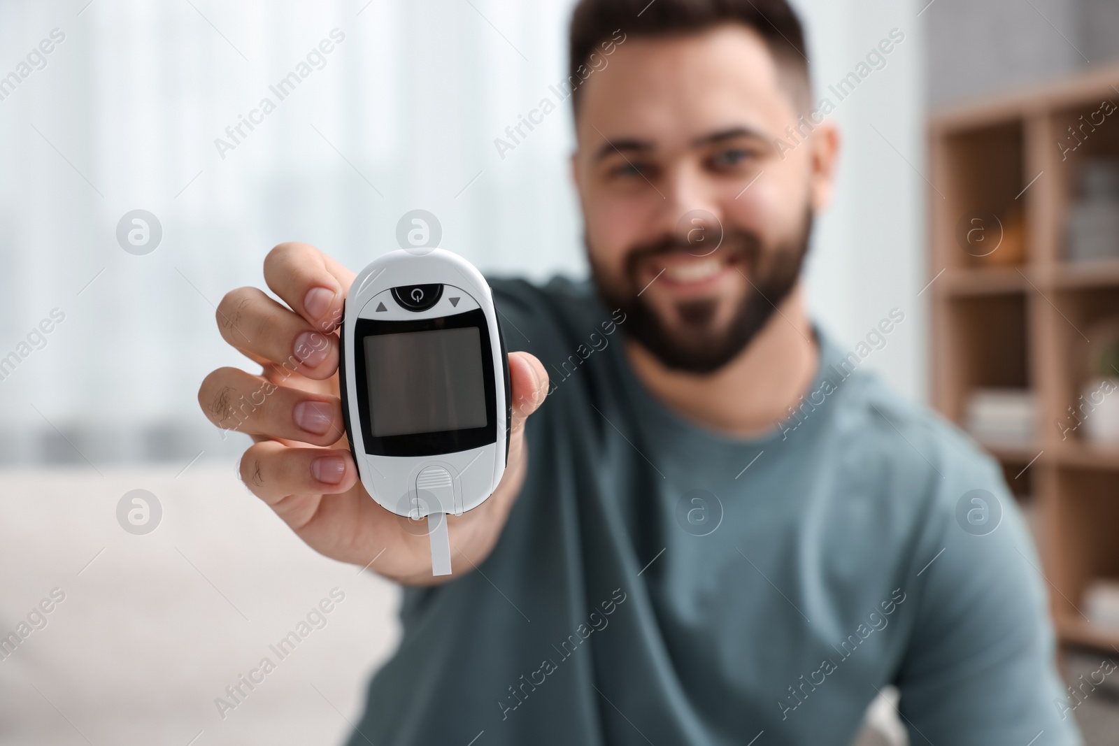 Photo of Diabetes test. Smiling man showing glucometer at home, selective focus