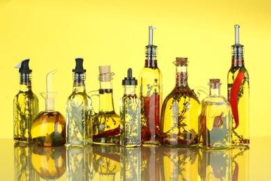 Photo of Cooking oil with different spices and herbs in bottles on yellow background