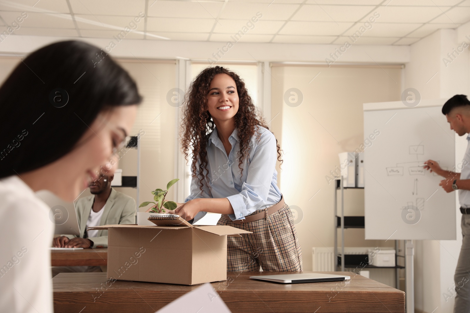 Photo of New coworker unpacking box with personal items at workplace in office