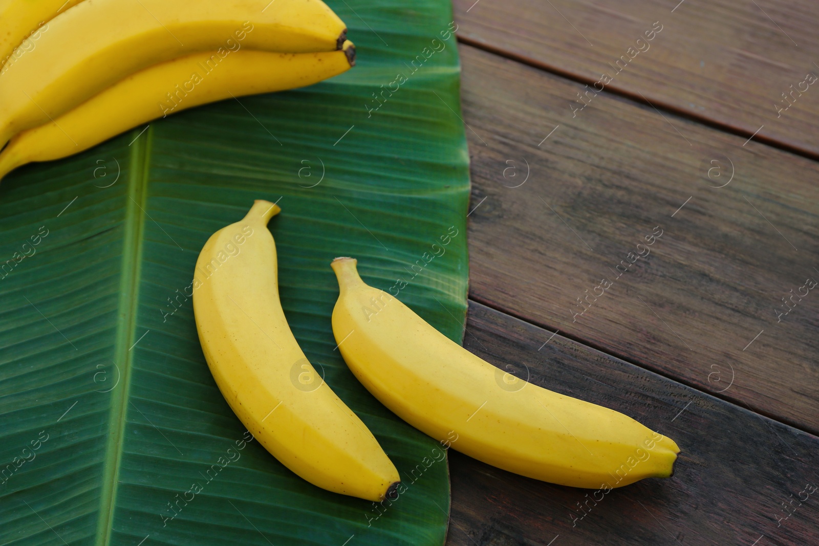 Photo of Delicious bananas and green leaf on wooden table, above view. Space for text