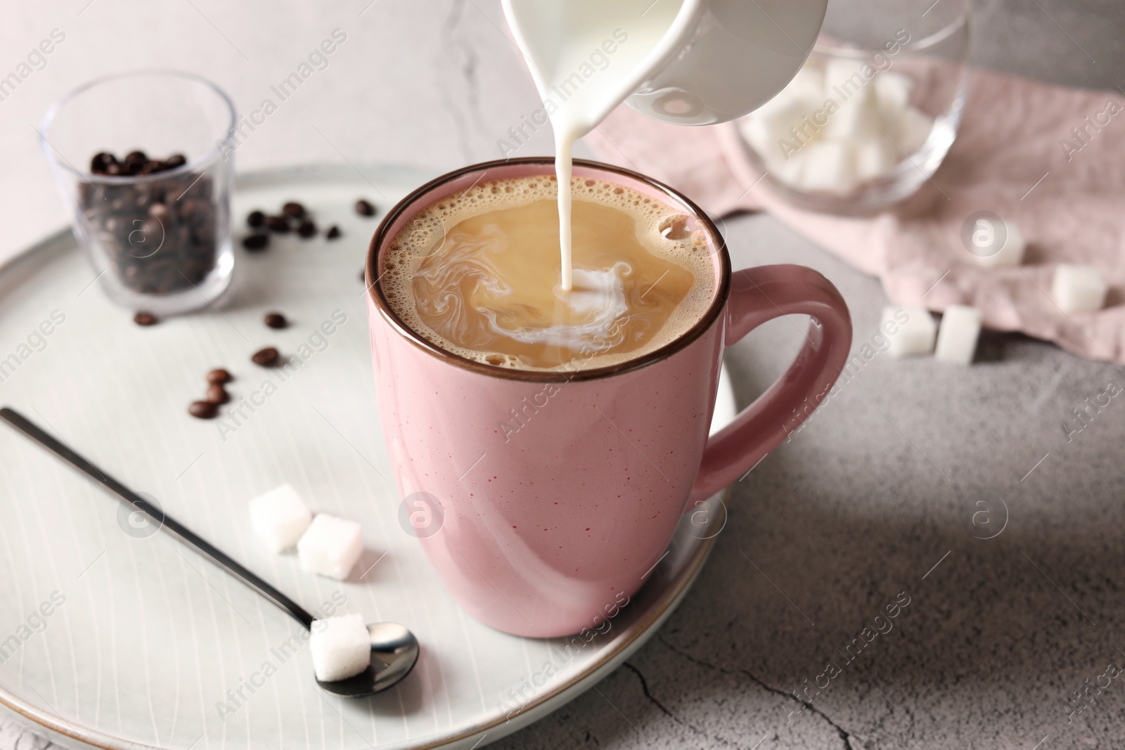 Photo of Pouring milk into cup with coffee on light grey textured table, closeup