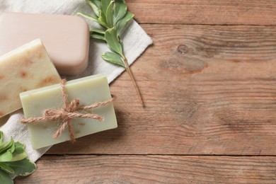 Soap bars and green plants on wooden table, flat lay. Space for text