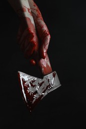 Man holding bloody axe on black background, closeup