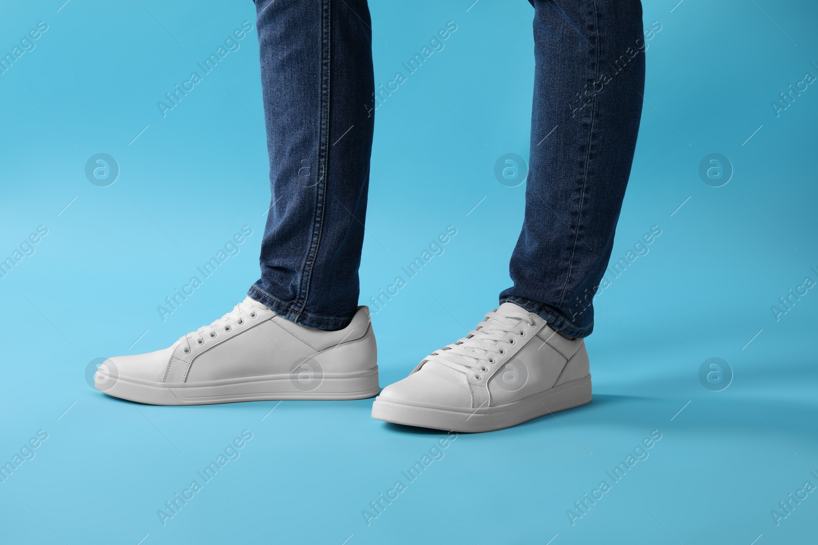 Photo of Man wearing stylish white sneakers on light blue background, closeup