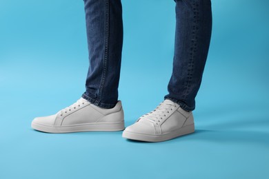 Photo of Man wearing stylish white sneakers on light blue background, closeup