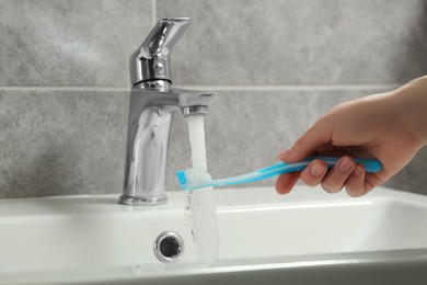 Photo of Woman washing plastic toothbrush under flowing water from faucet in bathroom, closeup