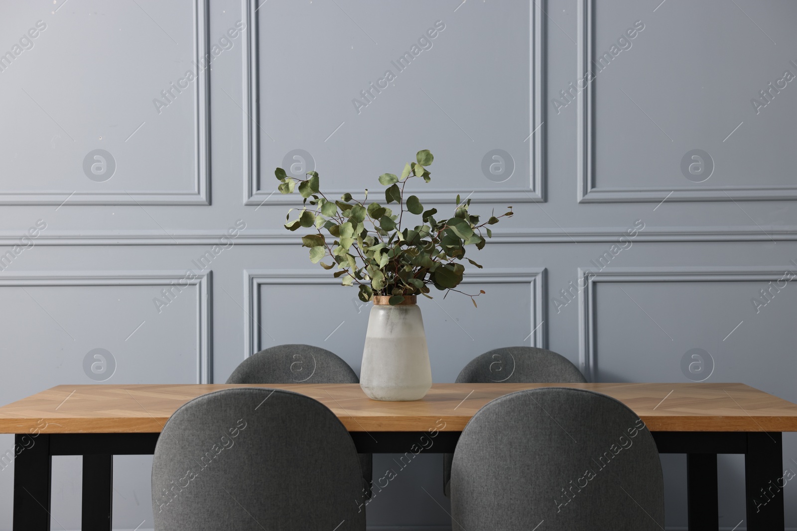 Photo of Soft chairs, table and vase with eucalyptus branches in stylish dining room