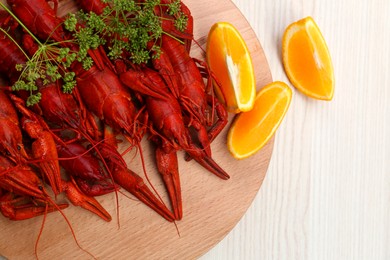 Photo of Delicious red boiled crayfish and orange on white wooden table, top view