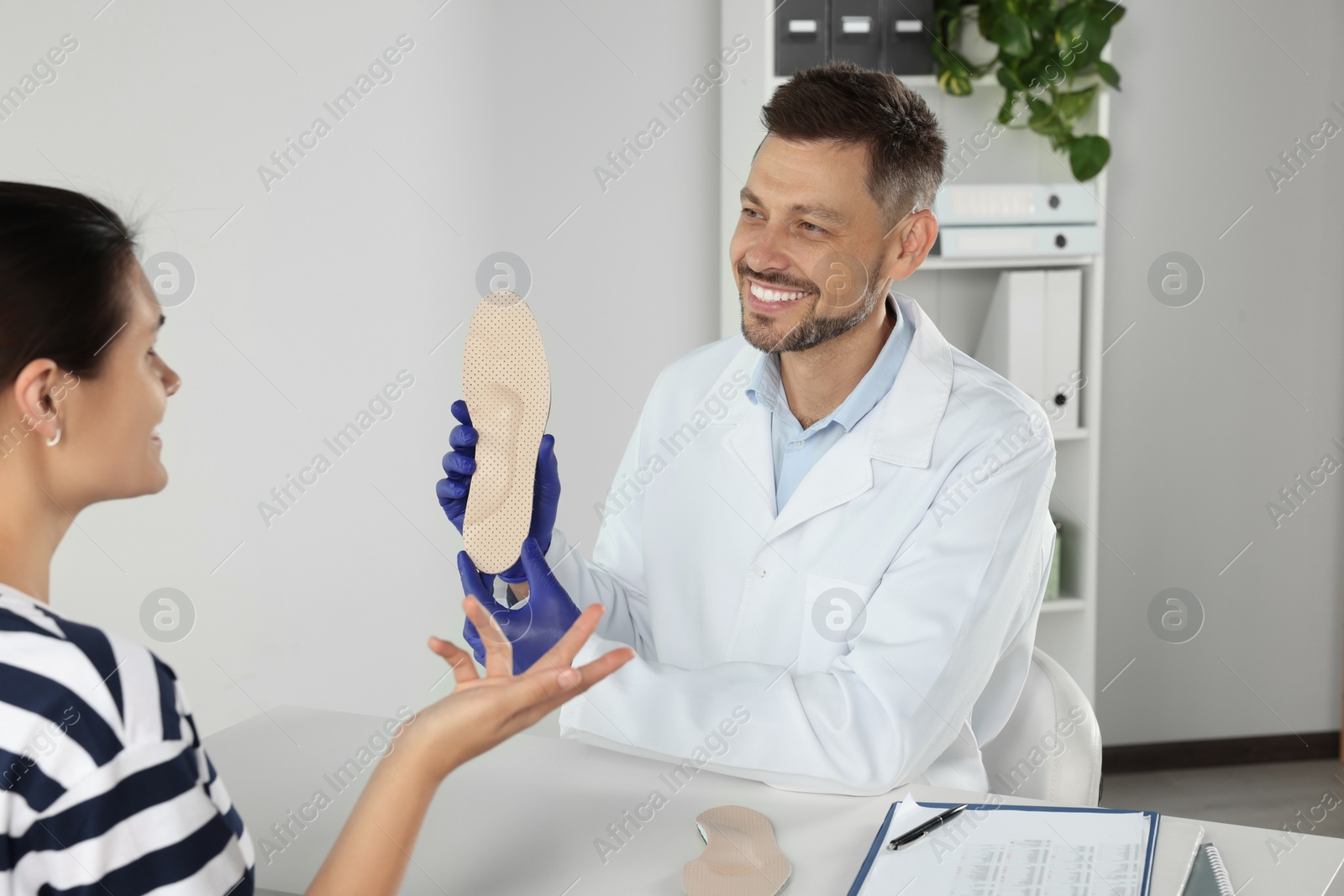 Photo of Handsome male orthopedist showing insole to patient in hospital