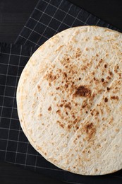 Photo of Many tasty homemade tortillas on black wooden table, top view
