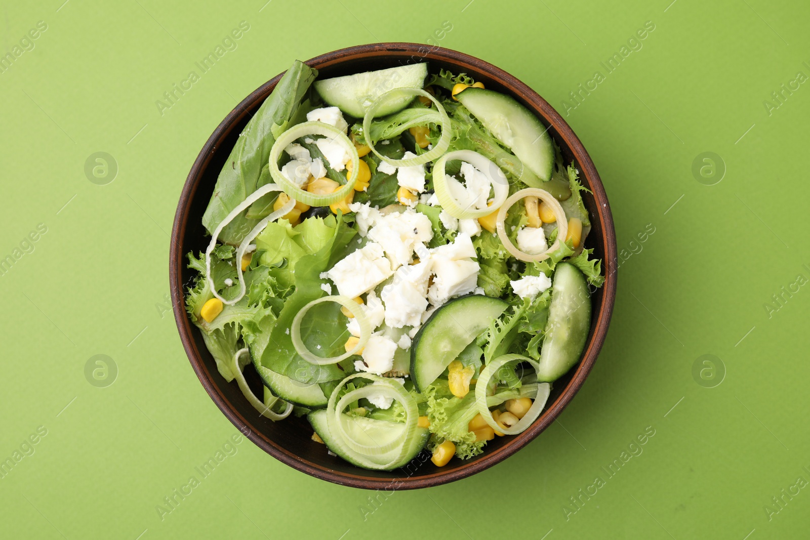Photo of Bowl of tasty salad with leek and cheese on green table, top view