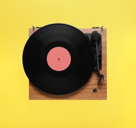 Photo of Modern turntable with vinyl record on yellow background, top view