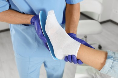 Male orthopedist fitting insole to patient's foot in hospital, closeup