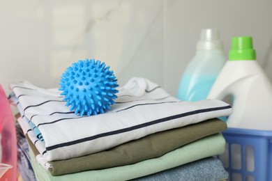 Photo of Blue dryer ball on stacked clean clothes near detergents
