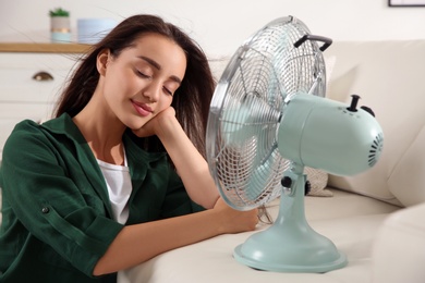 Photo of Woman enjoying air flow from fan at home. Summer heat
