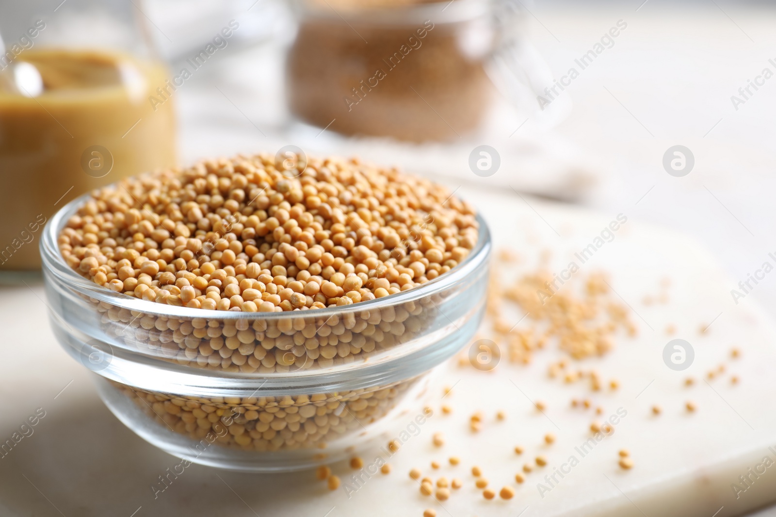 Photo of Mustard seeds in glass bowl on board, closeup. Space for text