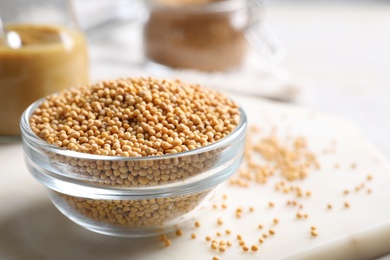 Photo of Mustard seeds in glass bowl on board, closeup. Space for text