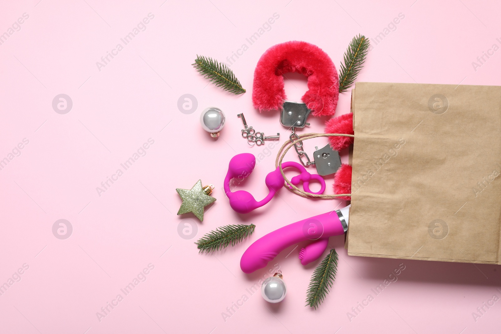Photo of Paper bag with different sex toys and Christmas balls on pink background, flat lay