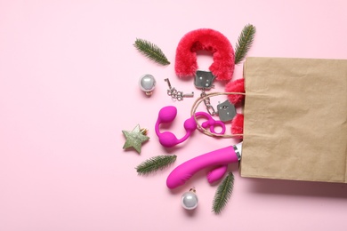 Paper bag with different sex toys and Christmas balls on pink background, flat lay