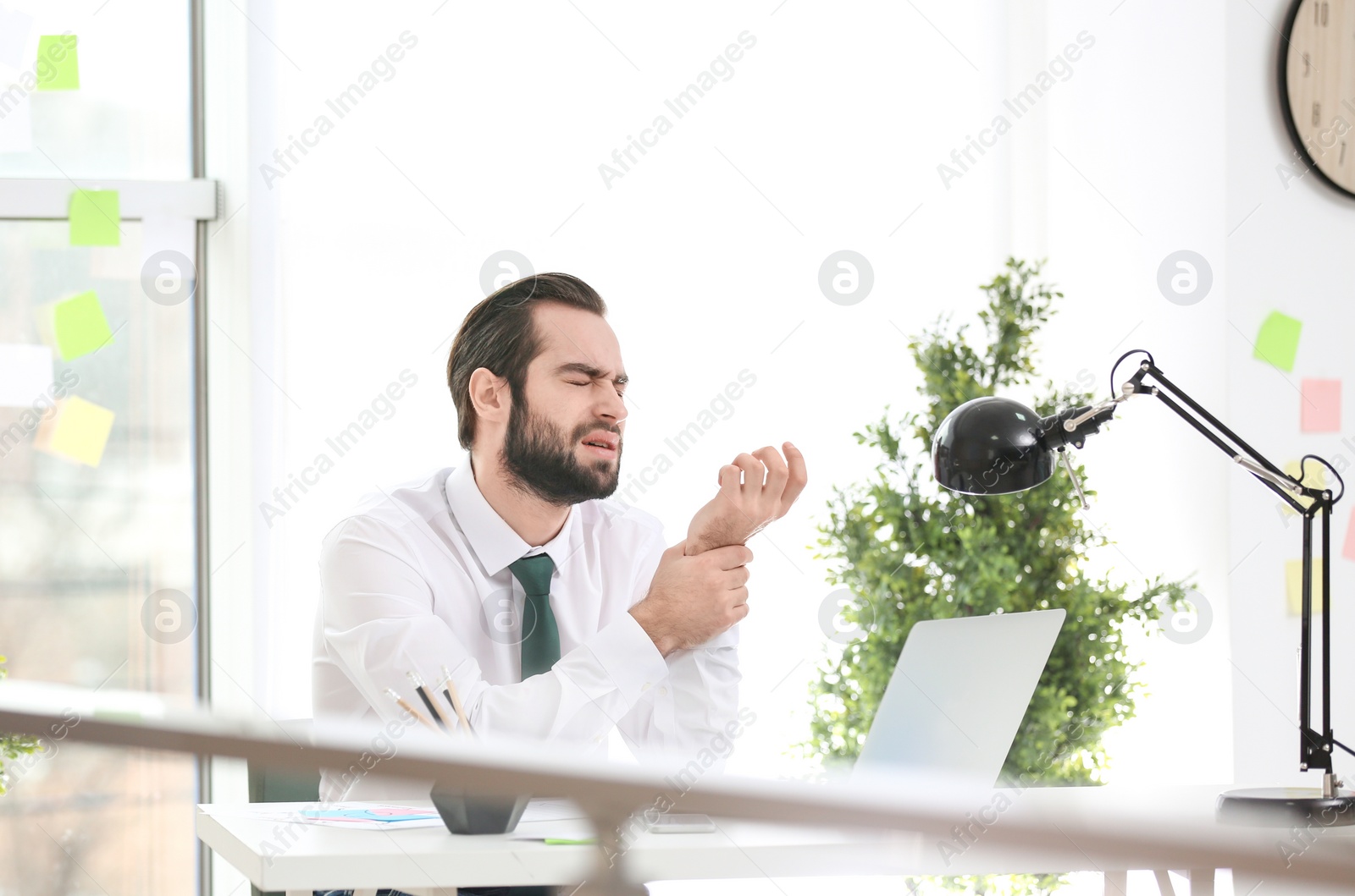 Photo of Young man suffering from wrist pain in office