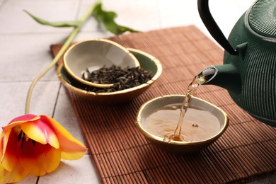 Photo of Traditional ceremony. Pouring brewed tea from teapot into cup on tiled table, closeup