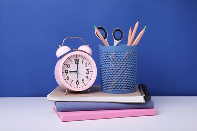 Photo of Different school stationery and alarm clock on white table against blue background. Back to school