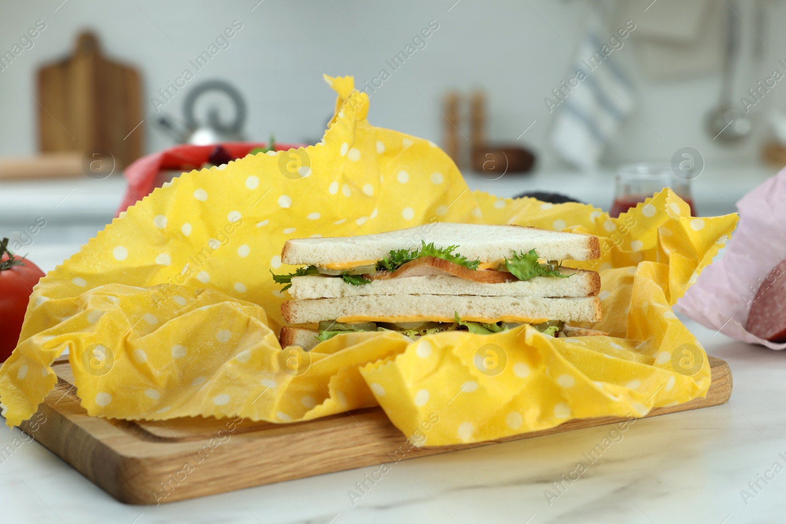 Photo of Tasty sandwich in beeswax food wrap on white marble table