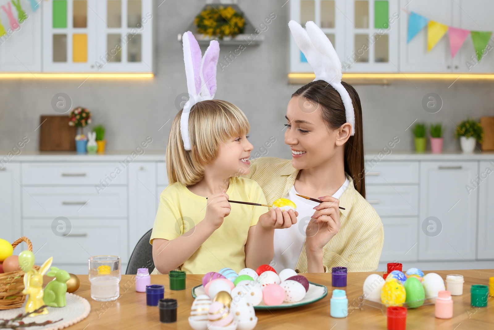 Photo of Mother and her cute son painting Easter eggs at table in kitchen