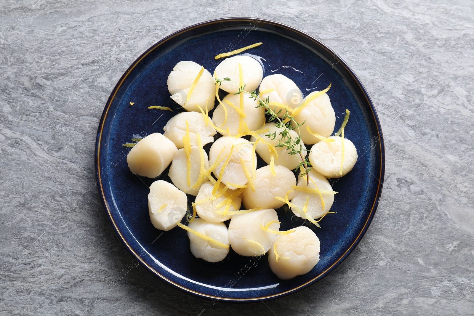 Photo of Raw scallops with thyme and lemon zest on grey marble table, top view