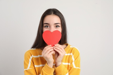 Photo of Portrait of beautiful young woman with paper heart on light background
