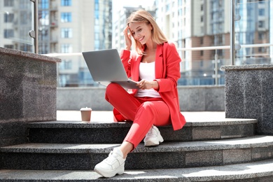 Photo of Beautiful businesswoman with laptop sitting on stairs outdoors