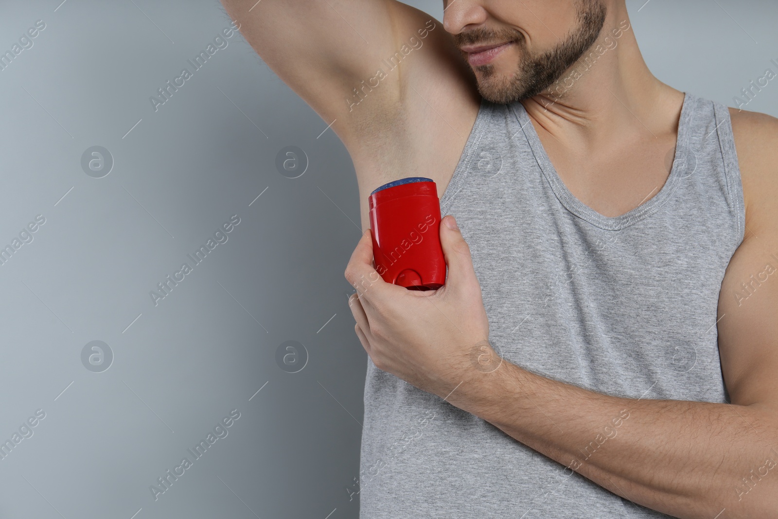 Photo of Man applying deodorant on grey background, closeup. Space for text