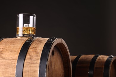 Photo of Whiskey with ice cubes in glass on wooden barrel against dark background, space for text