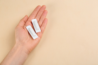 Photo of Closeup view of woman holding suppositories on beige background, space for text. Hemorrhoid treatment