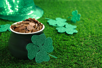 Photo of Pot of gold coins and clover on green grass, space for text. St. Patrick's Day celebration