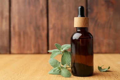 Photo of Bottle of mint essential oil and fresh herb on wooden table, space for text