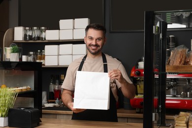 Happy worker with paper bag at desk in his cafe