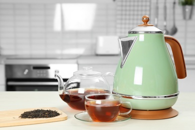 Photo of Modern electric kettle, teapot and cup on white wooden table in kitchen